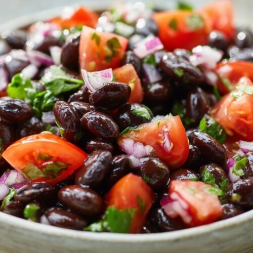 A bowl filled with black beans, chopped tomatoes, red onions, and fresh coriander leaves.