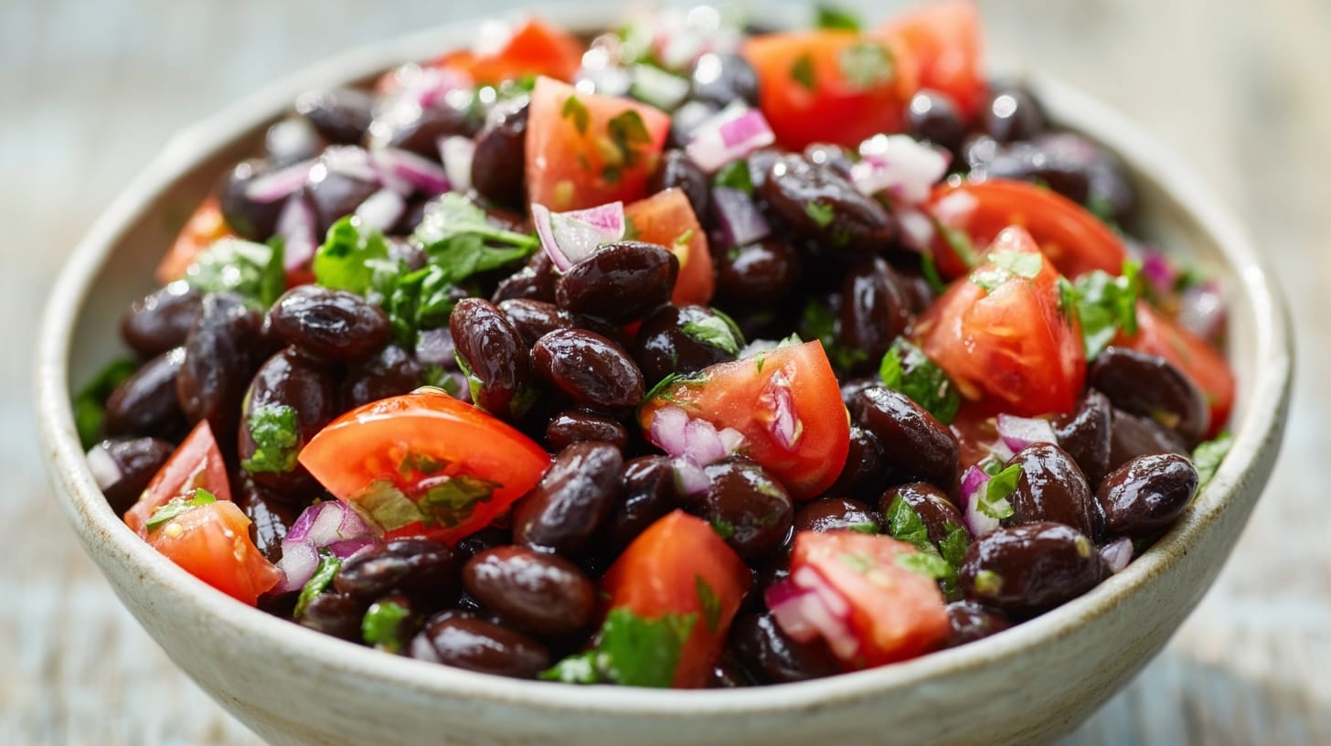 A bowl filled with black beans, chopped tomatoes, red onions, and fresh coriander leaves.