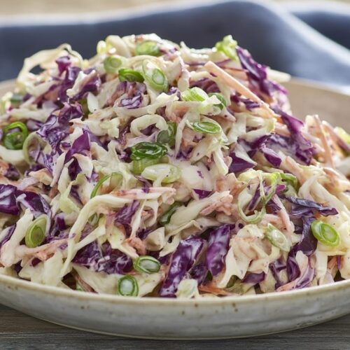 A bowl of cabbage slaw featuring shredded green and purple cabbage mixed with chopped spring onions.