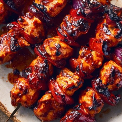 Grilled chicken skewers with a honey lime garlic glaze, garnished with red onion and served on a plate.