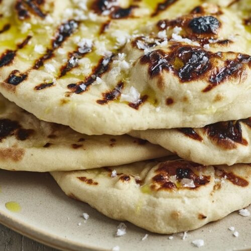 Three grilled flatbreads stacked on a plate, drizzled with olive oil and sprinkled with sea salt.