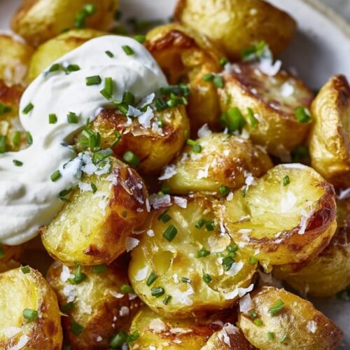 Golden roast potatoes topped with a dollop of soured cream and chopped chives on a plate.