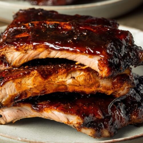 Three stacked pork ribs glazed with a dark, sticky sauce on a white plate.