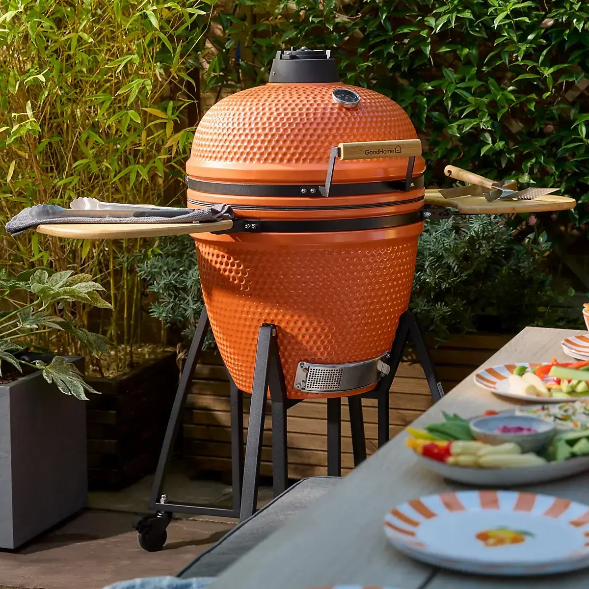 Orange ceramic egg-shaped barbecue grill with side tables in a garden setting.