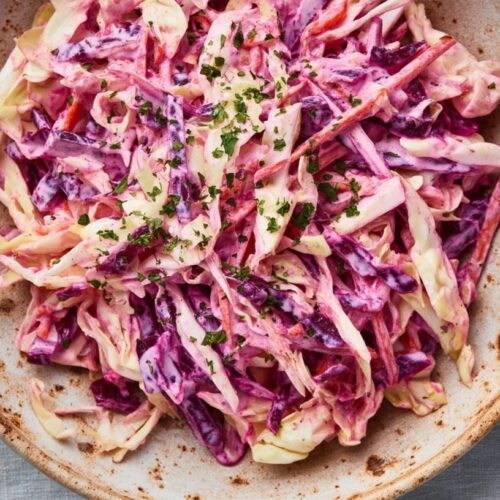 A bowl of coleslaw featuring shredded beetroot, carrot, and cabbage mixed with a creamy dressing.
