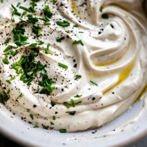Creamy dip with a smooth texture, garnished with chopped herbs and black pepper.