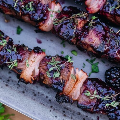 Grilled beef skewers glazed with blackberry chipotle sauce, garnished with thyme and shallots.