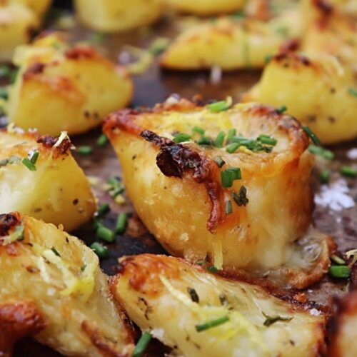 Golden brown crispy potatoes topped with green chives and lemon zest on a baking tray.