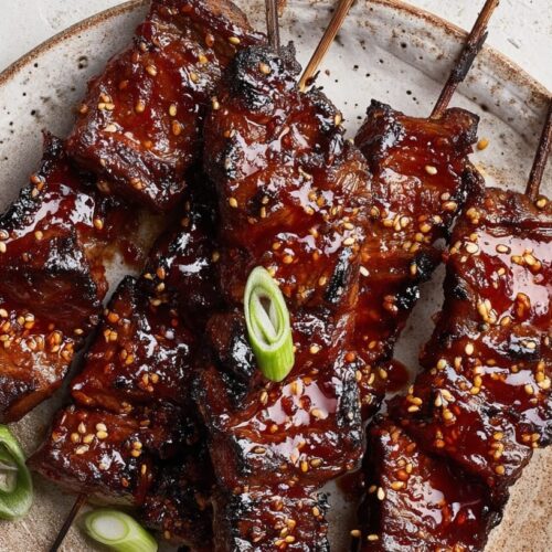 Grilled beef skewers glazed with gochujang honey sauce, garnished with sesame seeds and green onions.
