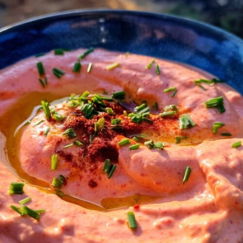 A bowl of Greek yoghurt dip with a pink hue, topped with olive oil and herbs.