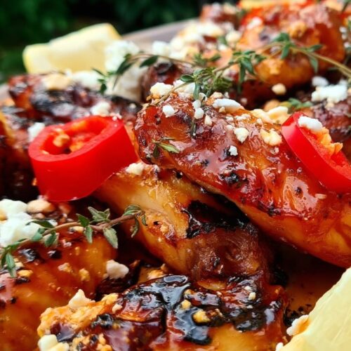 A plate of chicken wings topped with feta, chilli, thyme, and lemon wedges.