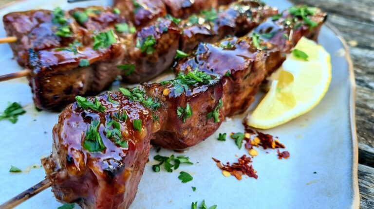 Grilled beef skewers glazed with honey garlic sauce, garnished with parsley and lemon slices.
