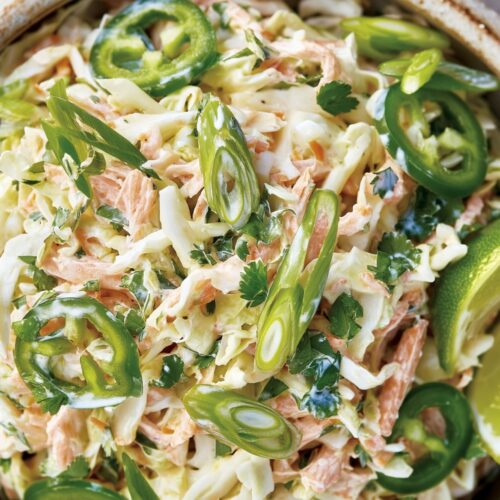 A bowl of coleslaw with shredded cabbage, jalape&ntilde;os, lime wedges, and coriander leaves.