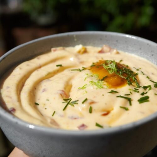 A bowl of creamy dip with a smooth texture, garnished with herbs and a drizzle of sauce.