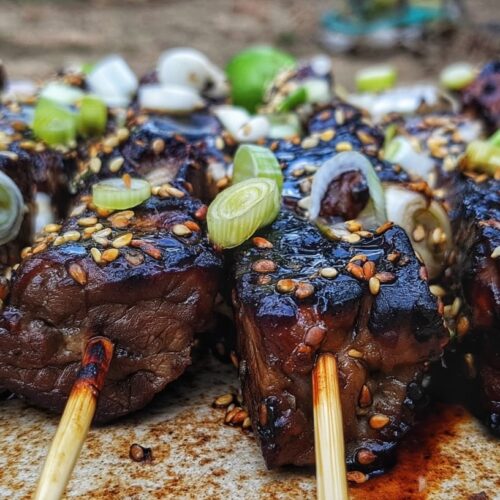 Grilled beef skewers coated with sesame seeds and topped with chopped green onions.