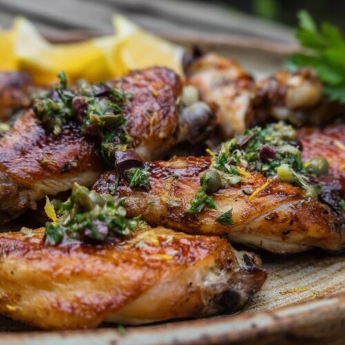 Golden-brown chicken wings garnished with parsley, capers, and lemon on a rustic plate.