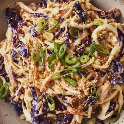 A bowl of coleslaw made with shredded cabbage, peanuts, and green onions on top.