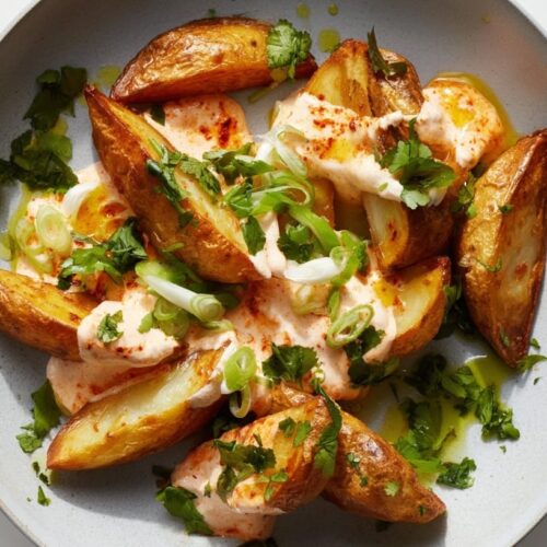 Golden brown potato wedges topped with creamy sauce and fresh green herbs on a plate.