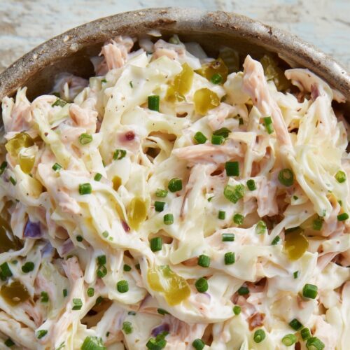 A bowl of coleslaw with shredded cabbage, smoked onion pickle, and chopped chives on a wooden surface.
