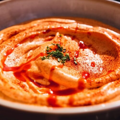 A creamy dip with a swirl of smoked paprika and Sriracha sauce, garnished with herbs.