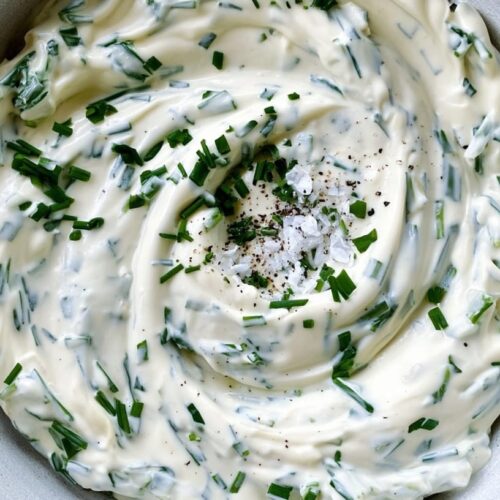 A creamy dip with a smooth texture, garnished with chopped chives and black pepper.