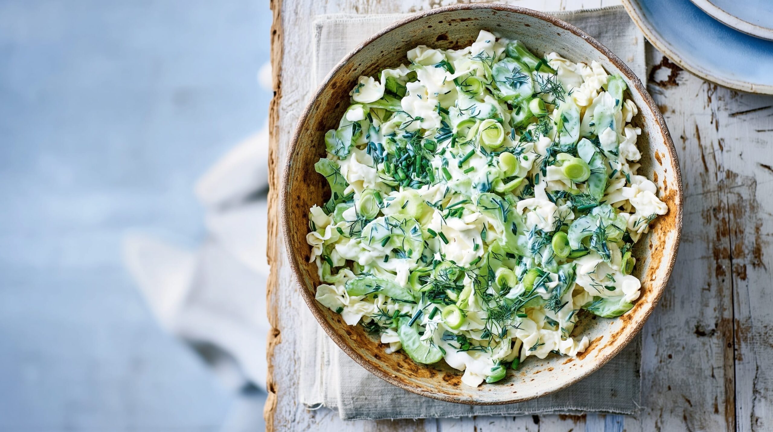 Bowl of coleslaw salad with spring onions, celery, and dill on a wooden table.
