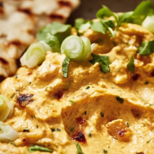 A bowl of creamy dip with charred pineapple, herbs, and green onions, served with flatbread.