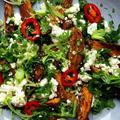 Roasted sweet potato wedges topped with feta cheese, chilli, lime, and coriander on a grey plate.
