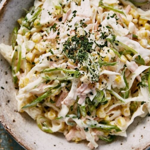A bowl of coleslaw salad with sweetcorn, scallions, and creamy dressing topped with herbs.