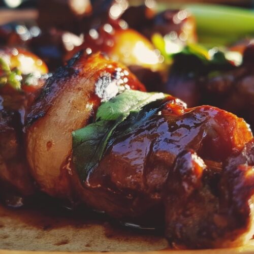 Grilled beef skewers glazed with a dark sauce, garnished with green herbs and shallots.