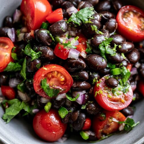 A bowl of black bean salad with cherry tomatoes, red onion, and fresh herbs.