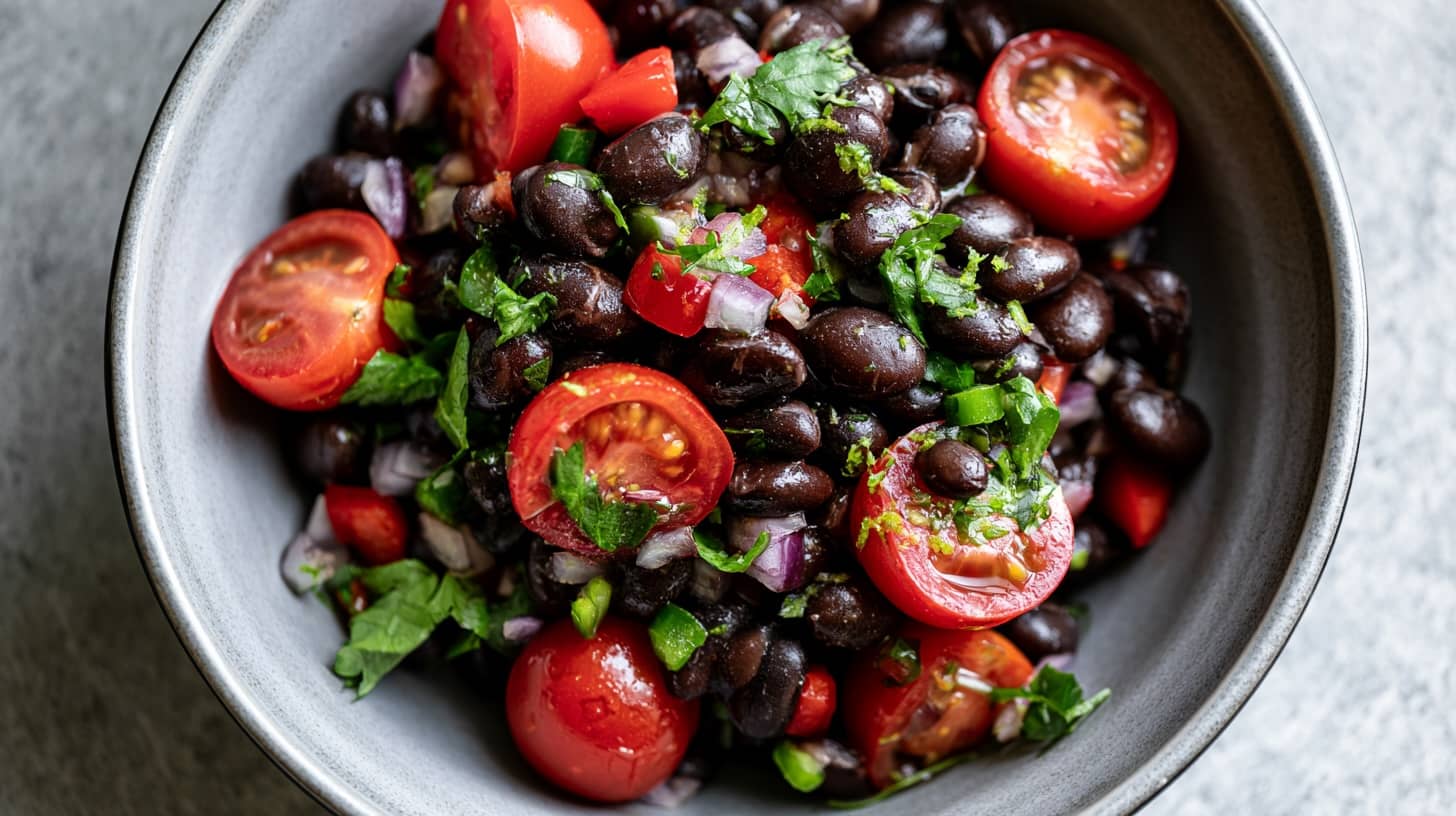 A bowl of black bean salad with cherry tomatoes, red onion, and fresh herbs.