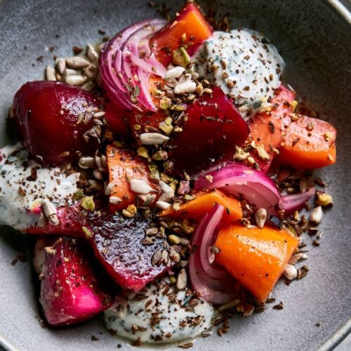 A bowl of cumin beetroot and carrot salad topped with mint yoghurt and seeds.
