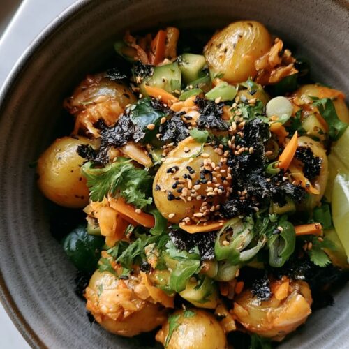 A bowl of kimchi sesame potato salad with cucumber, nori, and lime wedges on the side.