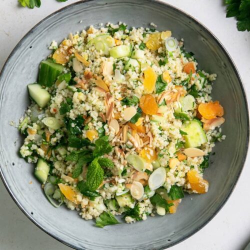 Bowl of lemon couscous salad with parsley, almonds, herbs, cucumber, and orange pieces