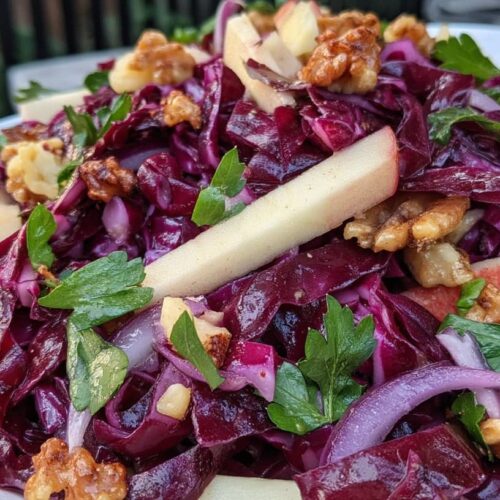 A vibrant salad featuring red cabbage, apple slices, walnuts, and fresh herbs on a white plate.