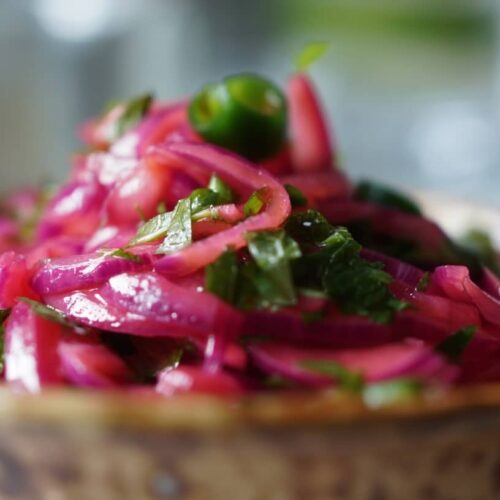 A bowl filled with pickled red onions, lime, and coriander, garnished with fresh herbs.