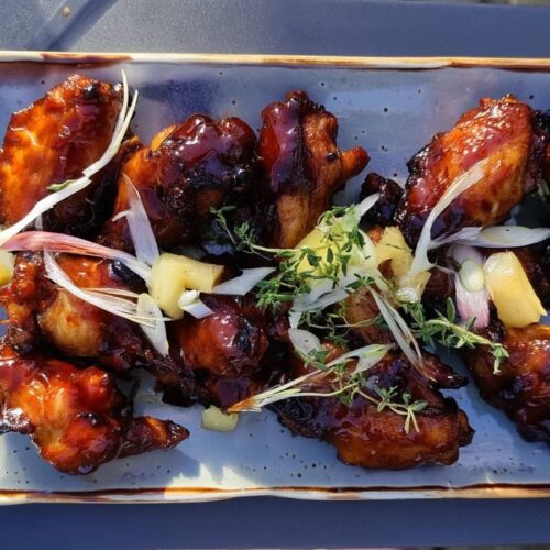 A plate of glazed chicken wings garnished with herbs and pineapple pieces on a blue dish.