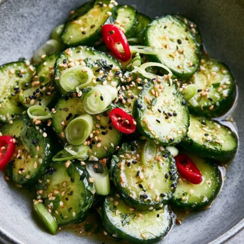 Sliced cucumbers topped with sesame seeds, spring onions, and red chillies in a bowl