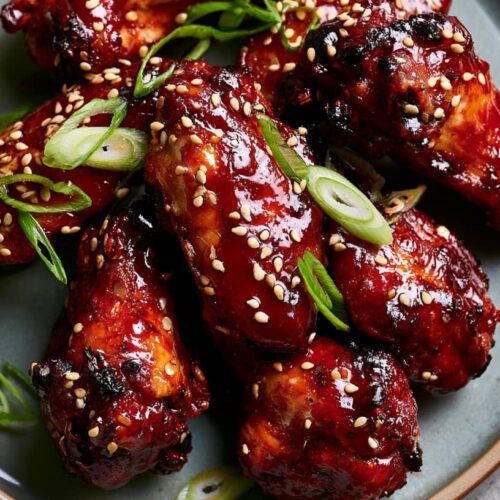 Sticky gochujang sesame chicken wings garnished with sliced spring onions and sesame seeds on a plate.
