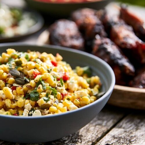 A bowl of sweetcorn salad with feta, lime, chilli, and coriander on a wooden table.