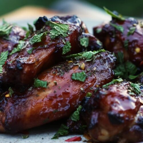 A plate of chicken wings coated in a dark glaze, garnished with fresh mint leaves.