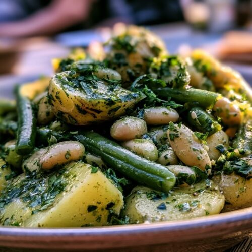 A bowl of warm potato bean salad with green beans and a chimichurri herb dressing, garnished with herbs.